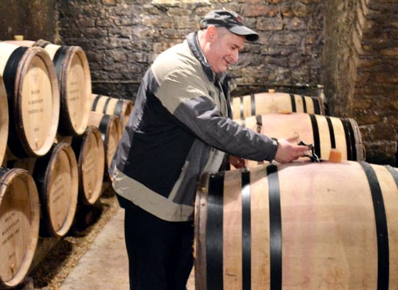 Person working beside oak barrels in a stone-walled Burgundy wine cellar