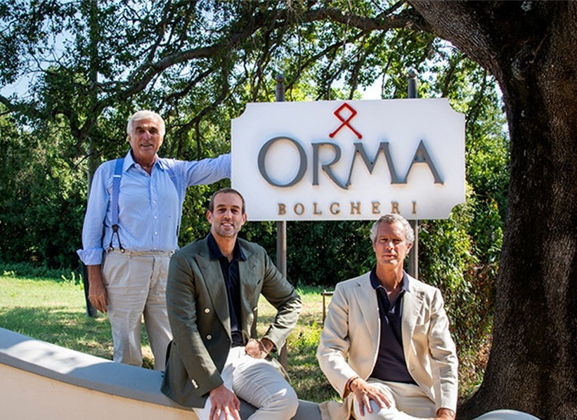 Three people at Orma Bolgheri with the complete winery sign visible under the trees